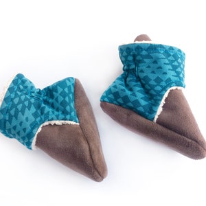 May include: A pair of brown and blue baby booties with a geometric pattern. The booties are made of soft, fuzzy fabric and have a fleece lining.