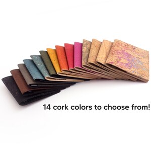 Pu&ograve; includere: Una collezione di 14 portafogli in sughero di vari colori, disposti a ventaglio su sfondo bianco. I colori includono nero, marrone, blu, verde, giallo, arancione, rosso e rosa. Il testo "14 colori di sughero tra cui scegliere!" &egrave; visualizzato.