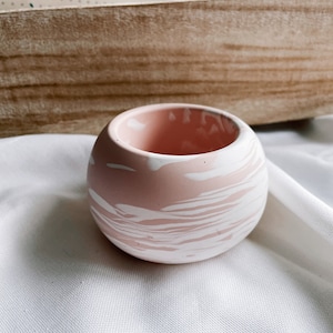 Könnte beinhalten: Ein kleiner, rosa-weißer, marmorierter Keramik-Pflanztopf. Der Topf hat eine glatte, abgerundete Form und einen weißen Rand.