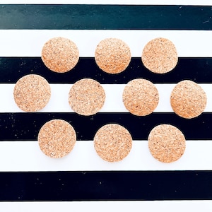 May include: Ten round cork coasters in a natural brown colour, arranged in a pattern on a black and white striped background.