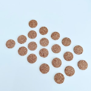 Puede incluir: Una colección de 20 círculos de corcho marrón dispuestos en un patrón diagonal sobre un fondo blanco.
