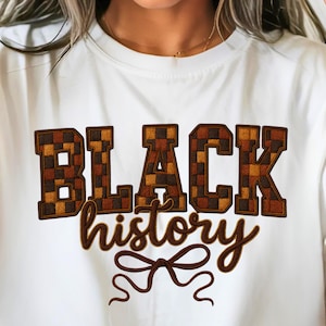 May include: White t-shirt featuring the words "BLACK history" in brown, checkered block letters and a cursive font. A brown bow design is below the text. The shirt is a casual style.