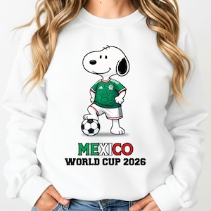 May include: White sweatshirt featuring a cartoon Snoopy character wearing a green and white soccer uniform, standing on a soccer ball. The text "MEXICO WORLD CUP 2026" is printed below the character in green and red.