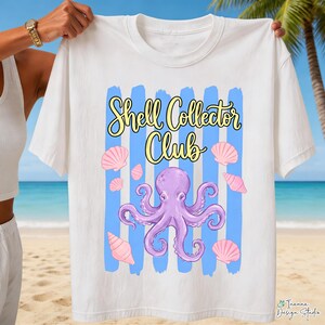 May include: White t-shirt with the text "Shell Collector Club" in yellow script. The design includes a purple octopus, pink seashells, and blue vertical stripes. The shirt is held up against a beach background.
