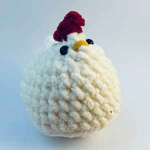May include: White crocheted chicken plush toy with a red pom-pom on top of its head, black eyes, and a yellow beak.