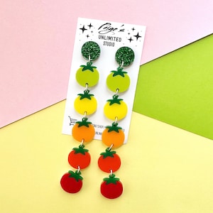 Può includere: Orecchini pendenti con un design a gradiente di pomodori. Gli orecchini presentano top glitterati verdi, seguiti da forme di pomodori verdi, gialli, arancioni e rossi. Sono attaccati a una carta bianca con il testo "Paige's Unlimited Studio."