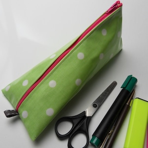 Può includere: Astuccio verde lime a pois bianchi con cerniera rosa. L'astuccio è aperto. Accanto all'astuccio ci sono forbici, penne e evidenziatori. Il tutto è su una superficie bianca.