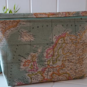 Könnte beinhalten: Rechteckige Reise-Kosmetiktasche mit Reißverschluss und Vintage-Kartenmuster. Die Tasche ist hellgrün mit einem türkisfarbenen Reißverschluss und einer detaillierten Karte in Beige, Braun und Rosa. Ideal für Reisen.