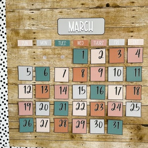 Pode incluir: Um calendário de madeira com um fundo rústico que mostra o mês de março. O calendário tem quadrados com os números de 1 a 31, cada quadrado tem uma cor diferente. As cores são pêssego, azul-petróleo, cinza e marrom. O calendário é decorado com bolinhas pretas e brancas.