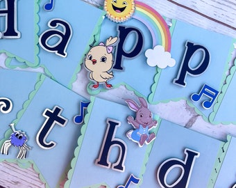 May include: A light blue banner spelling "Happy Birthday" with scalloped edges. The letters are dark blue with silver outlines. Decorative elements include a smiling sun, rainbow, musical notes, and cartoon animals.