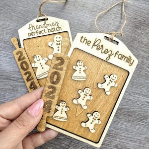 Könnte beinhalten: Zwei hölzerne Weihnachtsornamente mit Lebkuchenmännern und dem Text "Grandma's perfect batch" und "the Perez family".