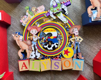 May include: A colorful Toy Story-themed birthday decoration featuring the characters Buzz Lightyear, Woody, Jessie, and others. The decoration includes the name "ALYSON" in block letters and a number "3" in the center, surrounded by a rainbow design.