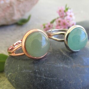May include: Two rings with green gemstone settings. One ring has a rose gold band and the other has a silver band.