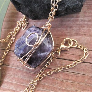 Puede incluir: Un collar de cadena dorada con un colgante de cristal de amatista p&uacute;rpura envuelto en alambre dorado.