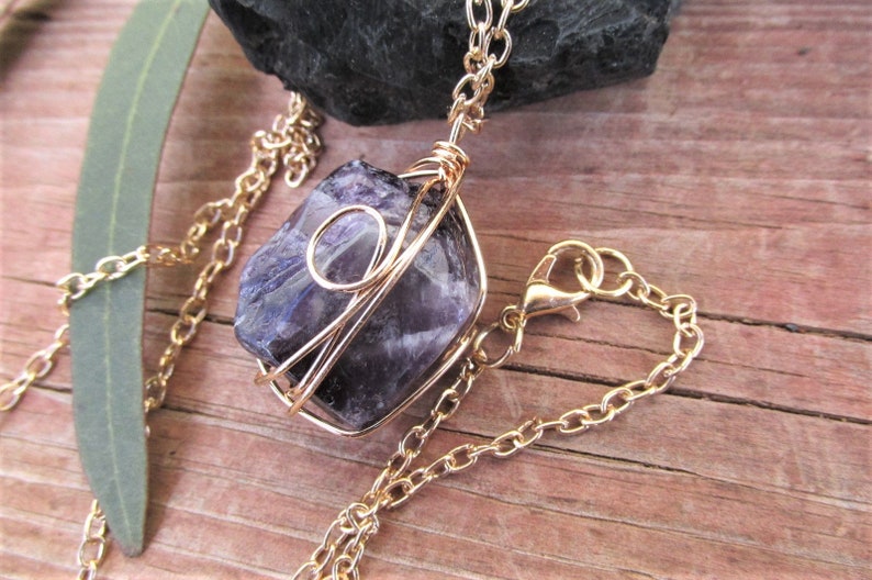 Puede incluir: Un collar de cadena dorada con un colgante de cristal de amatista p&uacute;rpura envuelto en alambre dorado.