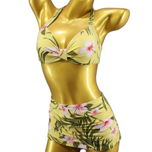 Può includere: Un bikini giallo con stampa floreale. La parte superiore è di stile halter con un fiocco sul davanti. La parte inferiore è una gonna a vita alta.