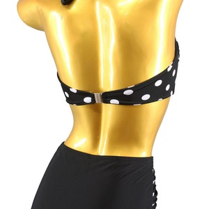 May include: Black and white polka dot bikini top with a black halter strap and a black high-waisted bottom. The bikini bottom has a cut-out detail on the side. The bikini is labeled "Aloha Beachwear".