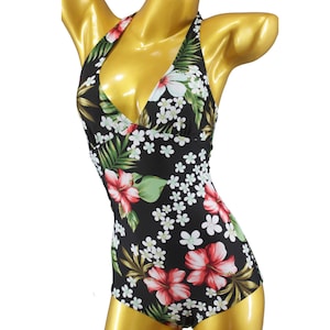 Può includere: Un costume da bagno nero con stampa floreale tropicale con fiori rossi, bianchi e verdi. Il costume da bagno ha uno stile halter e un'ampia scollatura.