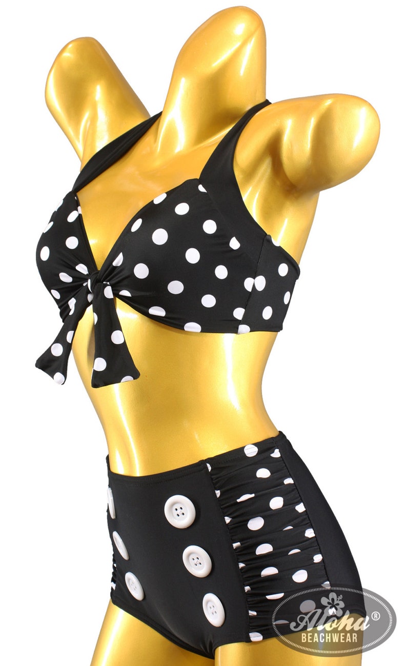 May include: Black and white polka dot bikini with a high-waisted bottom featuring white buttons. The top has a bow tie detail. The bikini is on a gold mannequin.