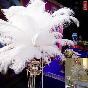 May include: A large, elegant centerpiece featuring a cluster of fluffy white feathers. The feathers are arranged atop a silver candelabra, with strings of pearls cascading down. The background includes a blue tablecloth and decorative elements.