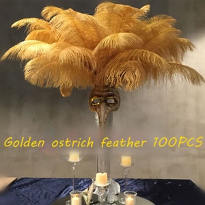 May include: A vase filled with 100 golden ostrich feathers. The vase is decorated with a masquerade mask. The text "Golden ostrich feather 100PCS" is visible in the image.