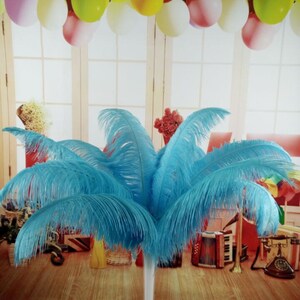 May include: A cluster of vibrant blue ostrich feathers arranged in a decorative display. The feathers are a bright turquoise color and are arranged to resemble a palm tree. The background includes colorful balloons and musical instruments.
