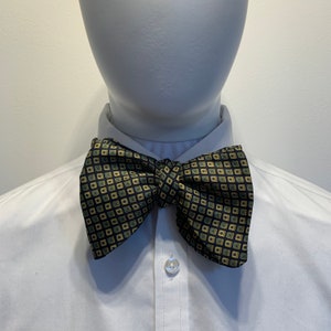 Könnte beinhalten: Eine schwarze Fliege mit einem geometrischen Muster aus kleinen gelben Quadraten auf schwarzem Hintergrund.