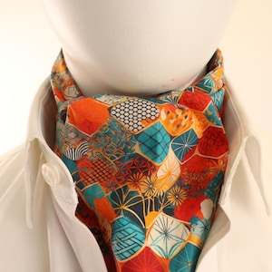 May include: A colorful ascot scarf with a geometric pattern in orange, teal, and white. The scarf is worn with a white collared shirt. The pattern includes various shapes and designs, creating a vibrant accessory.