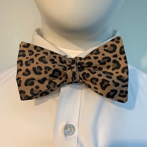 May include: A brown and black bow tie with a leopard print pattern.