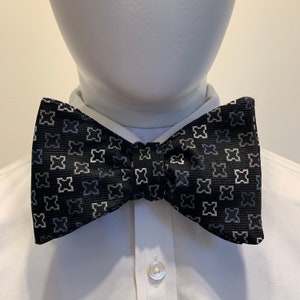 Könnte beinhalten: Eine schwarze Fliege mit einem weißen geometrischen Muster. Die Fliege ist aus einem strukturierten Stoff gefertigt.