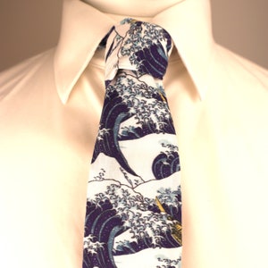 May include: A patterned necktie with a Japanese wave design in navy blue and white, knotted against a white shirt. The tie's design is inspired by the famous artwork "The Great Wave off Kanagawa". The intricate pattern and colour contrast are clearly visible.