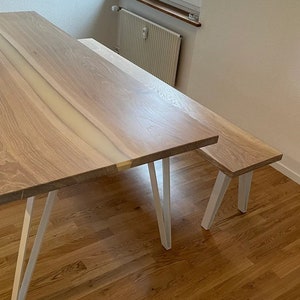 May include: A wooden table and bench set with white metal legs. The table top has a natural wood grain and a white resin inlay.