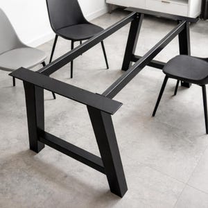 Op de afbeelding: Zwart metalen tafelonderstel met een rechthoekig frame en schuine poten. De basis is ontworpen voor een tafelblad en heeft een moderne, minimalistische stijl. Het tafelonderstel wordt getoond met drie zwarte stoelen.