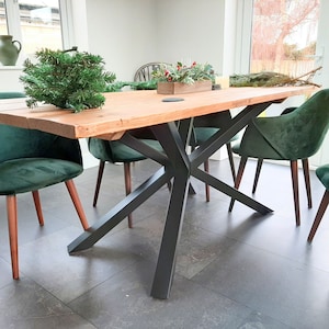 May include: A wooden dining table with a black metal base. The table has a rustic, reclaimed wood top and a modern, industrial style base. The table is surrounded by four chairs with green velvet upholstery.