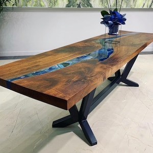 May include: A wooden dining table with a black metal base. The table top has a river of blue resin running through it.