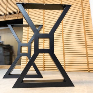 Könnte beinhalten: Zwei schwarze Metalltischbeine mit geometrischem Design. Die Beine sind X-förmig mit einem Quadrat in der Mitte. Die Beine stehen auf einem hellbraunen Holzboden.