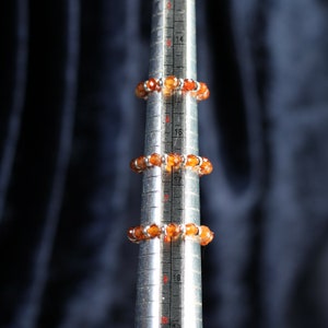 May include: Three orange gemstone rings on a metal ring sizer. The rings are made of small, round gemstones.