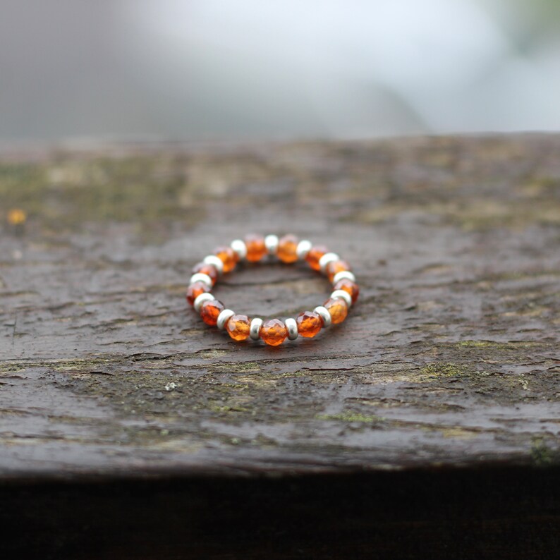 May include: A silver and orange beaded ring with small round beads.