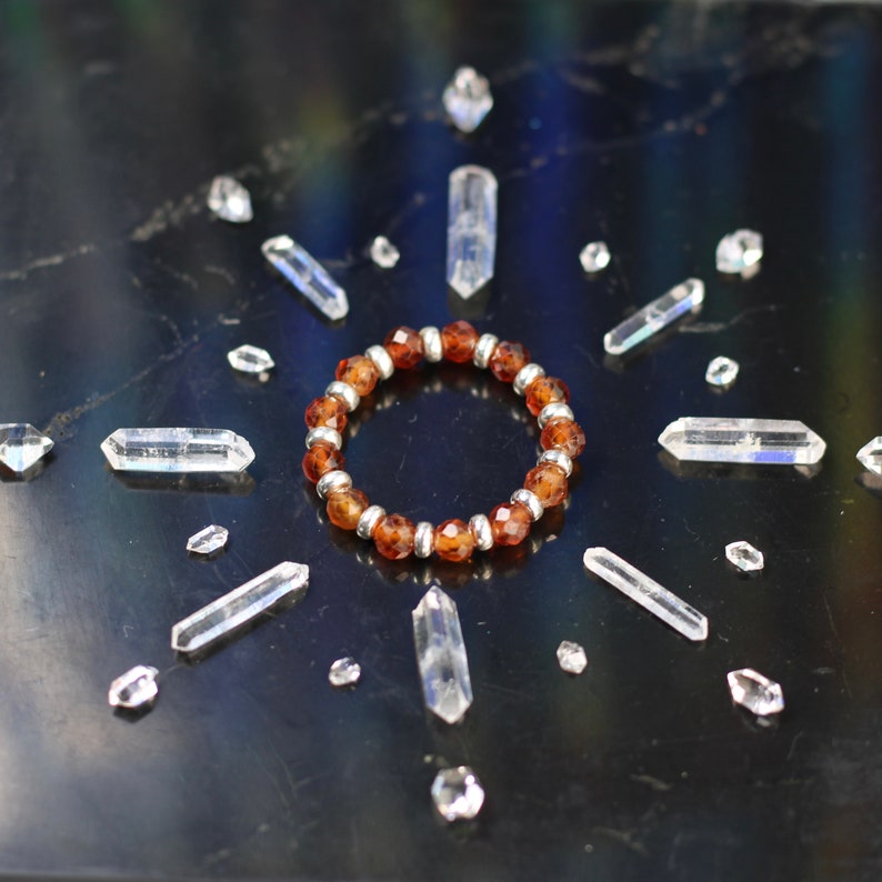 May include: A brown gemstone bracelet with silver beads, surrounded by clear quartz crystals on a black background.