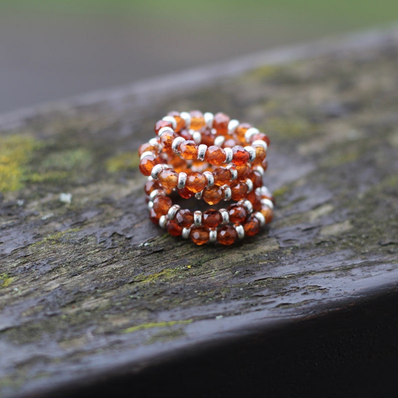 May include: A stack of four silver rings with orange gemstone beads. The rings are stacked on a wooden surface.