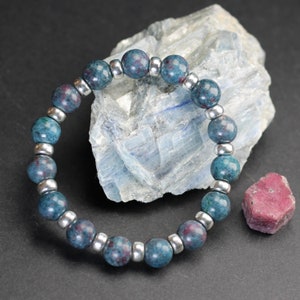 May include: A blue and silver beaded bracelet against a dark blue background. The bracelet is made of round beads with a speckled pattern and silver spacer beads.