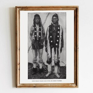 Könnte beinhalten: Gerahmter Schwarz-Weiß-Druck mit zwei indianischen Männern in traditioneller Kleidung. Die Männer tragen verzierte Kleidung, darunter offenbar Otter- und Hermelintrophäen. Der Druck befindet sich in einem Holzrahmen.