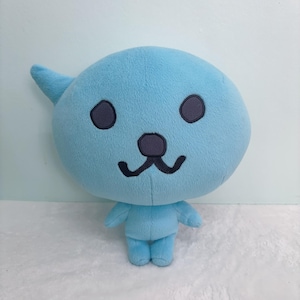 May include: A light blue plush toy shaped like a cartoon character with a large head, small body, and a single horn. The toy has black eyes, a grey nose, and a stitched-on smile.