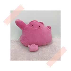 May include: A pink plush toy of the Pokemon,  Jigglypuff, with a smaller pink Jigglypuff plush toy in front of it.