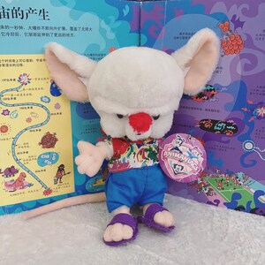 May include: A white plush toy of a cartoon mouse wearing a blue and multi-colored Hawaiian shirt and blue shorts. The mouse has a red nose and large ears. The toy is holding a tag that says "Animaniacs".
