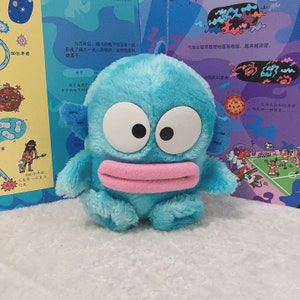 May include: A blue plush toy with large eyes and a pink mouth. The toy has a fuzzy texture and is shaped like a cartoon character.