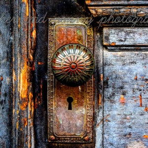 May include: A vintage door knob with a decorative, ornate design. The knob is made of brass and has a keyhole. The door is made of wood and has a weathered, distressed look.