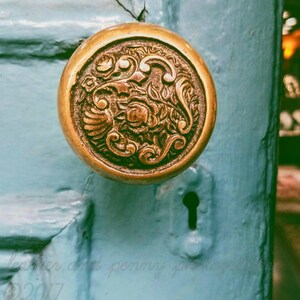 May include: A vintage brass door knob with an ornate floral design. The knob is mounted on a light blue door.