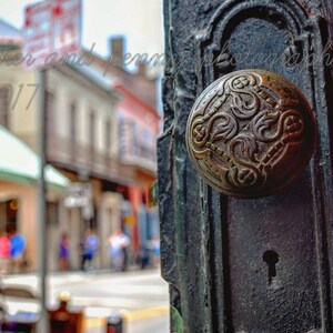 May include: A close-up of a vintage-style door knob with intricate floral designs. The knob is made of brass and has a dark patina. The door knob is attached to a wooden door with a red painted surface.
