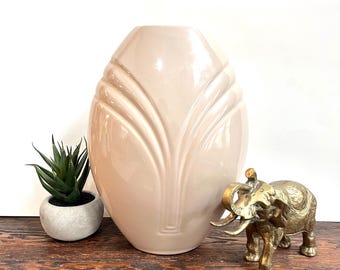 May include: A beige ceramic vase with a vertical, stylized leaf design. A small potted succulent and a brass elephant figurine are also present. The vase is approximately 12 inches tall.